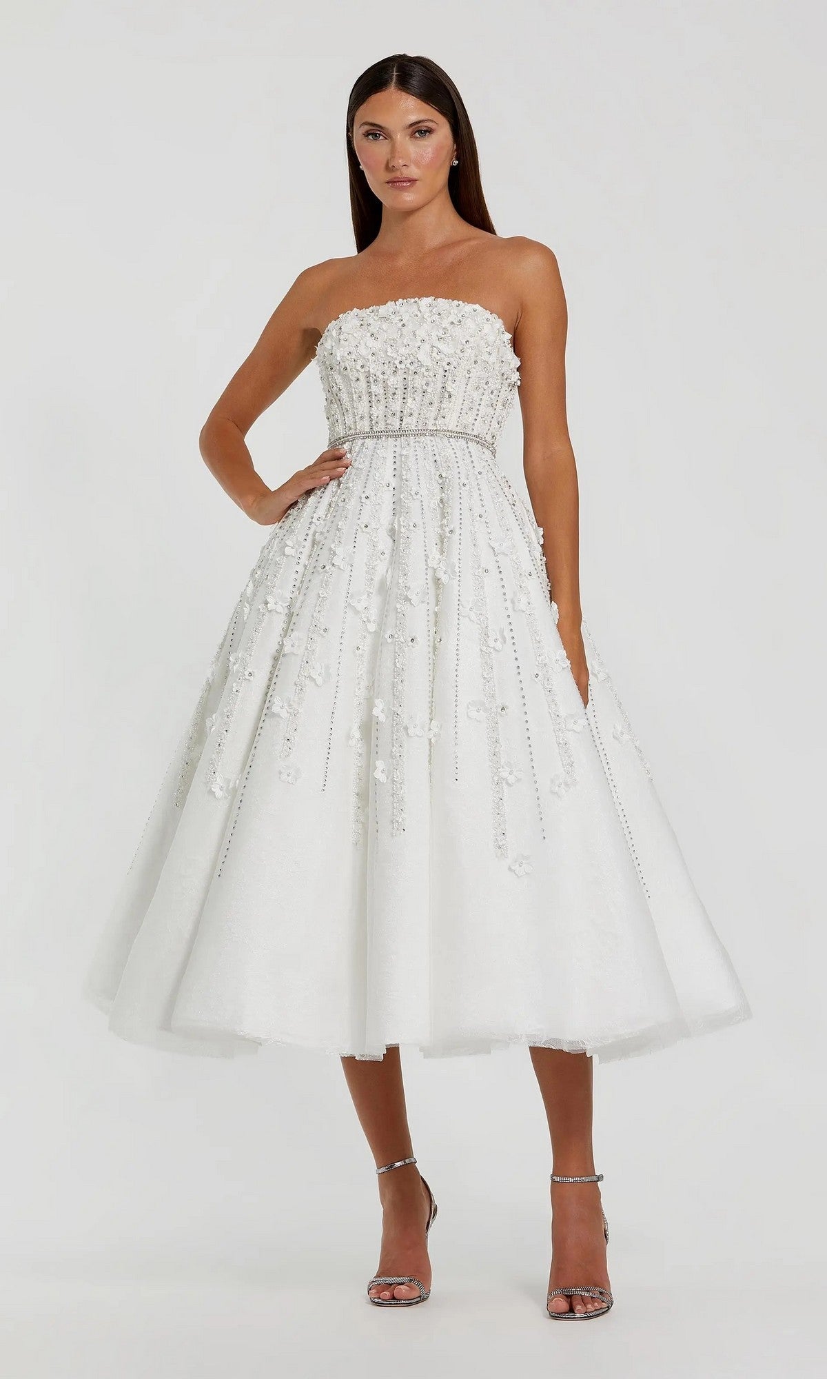 A woman wears the Strapless Champagne Party Dress: Mac Duggal 11865 with floral embellishments and silver heels, standing against a plain background. Ideal as a chic, semi-formal dress for any elegant occasion.